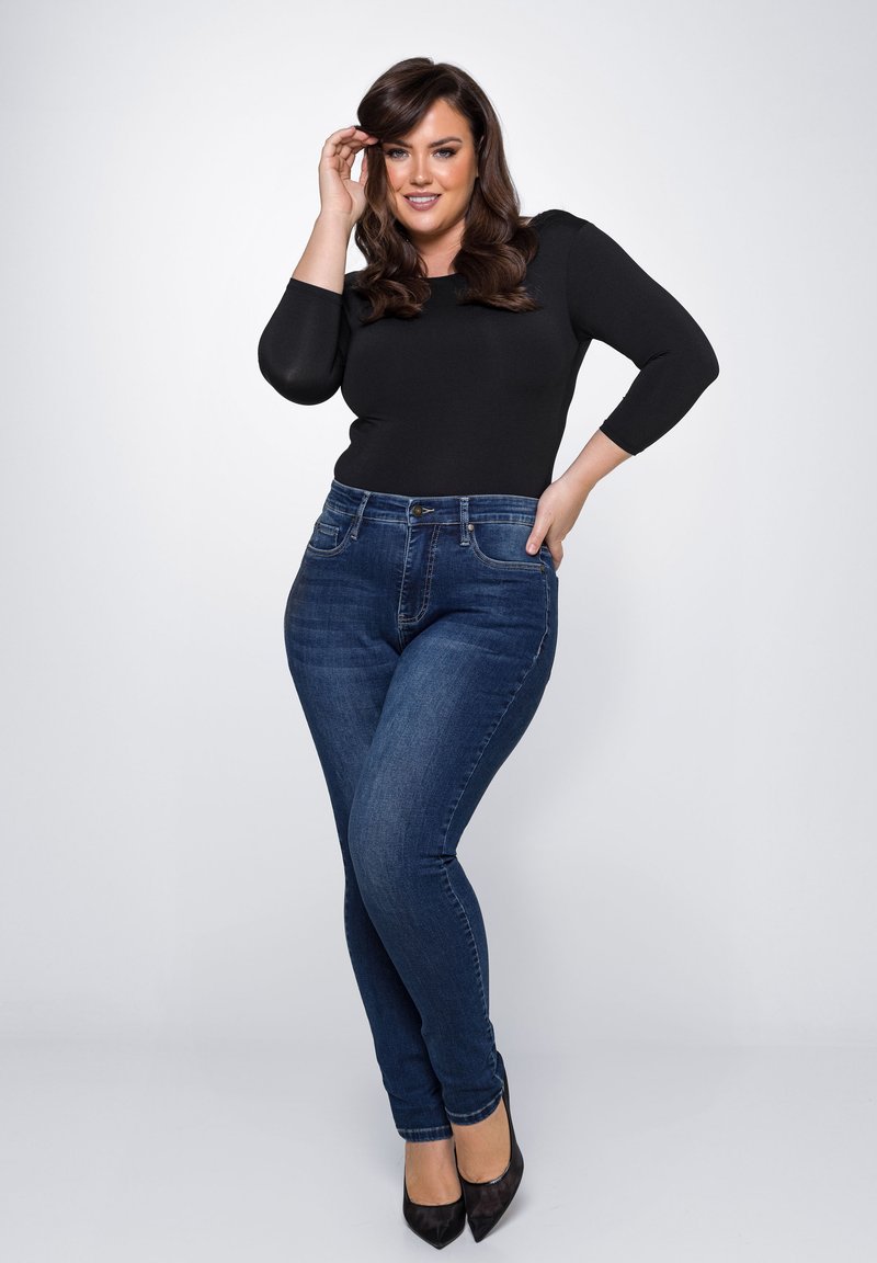 Zwarte getailleerde top en donkerblauwe skinny jeans van denim. De jeans hebben een klassiek vijfzakkenontwerp en een knoopsluiting.