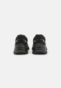 Chaussures de sport noires avec une texture lisse, des semelles rembourrées et des accents réfléchissants sur le talon. La vue arrière met en valeur le design et la forme.