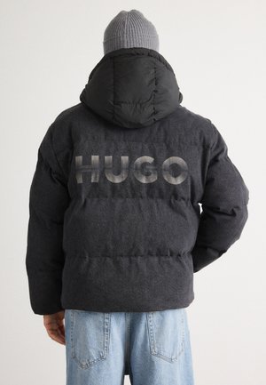 Fekete puffdzseki kapucnival, struktúrált anyagból készült, a hátsó részén nagy, világosszürke "HUGO" logóval.