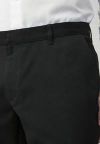 Musthave mustad, millel on sile ja tekstuuriga kangas, kitsas lõige, esiküljel taskud ja kootud mustrist tulenev kerge sära.