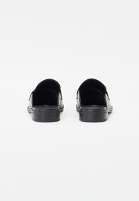Black slip-on shoes with a smooth leather finish, rounded back, low heel, and cushioned insoles. Minimalist design with no visible hardware.