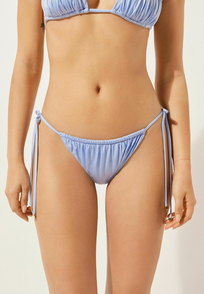Světle modré bikiny s nabíranými detaily, bočními zavázáním a hladkým povrchem. Obsahují nastavitelné popruhy pro přizpůsobitelné nošení.