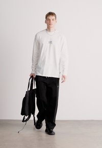 Λευκό πουκάμισο με μακριά μανίκια και γραφικά, μαύροι χαλαροί παντελόνες και μαύρο σακίδιο. Λείος υφασμάτινος ιστός, απλός σχεδιασμός, μινιμαλιστικό στυλ.