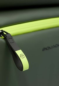 Donkergroene tas met een gestructureerde afwerking en een felgroene ritssluiting. De ritstreker heeft een zwarte accentuering en een logo detail.