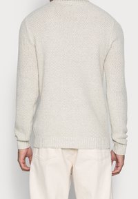 Ljust grå stickad tröja med ett texturerat mönster, ribbade ärmslut och fåll, rundad halsringning, sedd från baksidan.