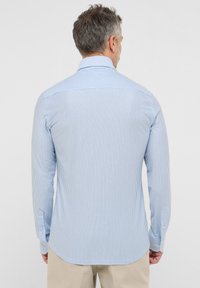 Camicia a maniche lunghe con un motivo a righe verticali blu chiaro e bianche, con colletto a punta e polsini abbottonati. Tessuto morbido.