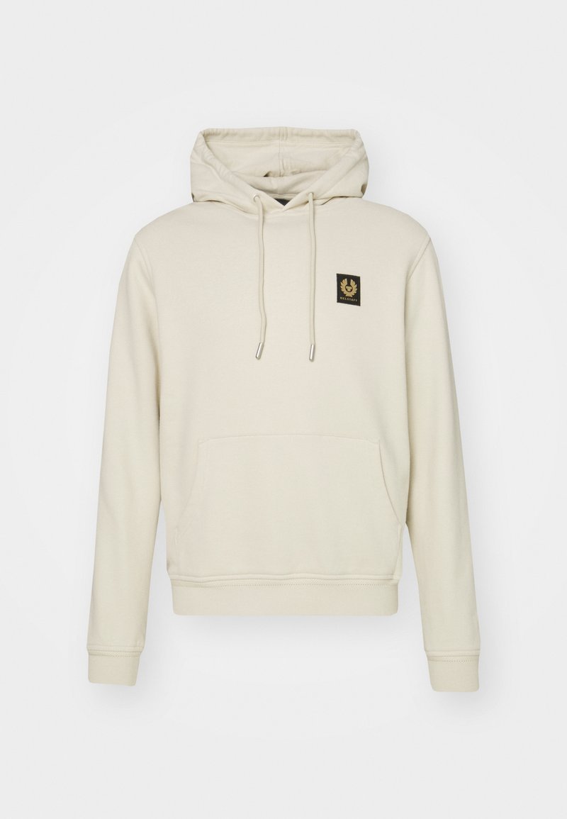 Beige huvtröja i mjukt tyg, med en ficka fram, dragsnören och en liten svart logotyp på bröstet.