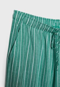 Pantalon à rayures verticales vertes et blanches avec taille élastique et cordon, montré de la taille à mi-cuisse sur fond blanc.