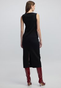 Zwarte mouwloze top met een ribbelstructuur, in combinatie met een bijpassende lange rok met een split aan de achterkant. Accessoires omvatten rode hoge hakken.