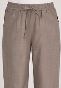 Lichtbruine, gestreepte broek met een elastische tailleband en een trekkoordsluiting. Heeft een gladde, zachte textuur en een losse pasvorm.