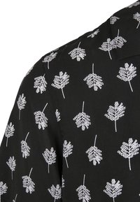Chemise en tissu noir avec un motif de feuilles blanches, détails brodés, texture lisse et col classique.