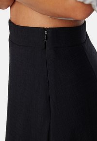 Svarta högmidjade byxor i ett strukturerat tyg, med en diskret dragkedja bak och rena, skräddarsydda linjer.