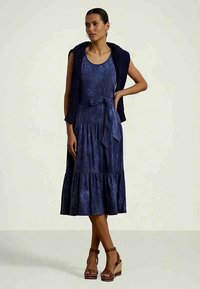 Tamsiai mėlyna be rankovių suknelė su rišama juosmeniu ir sluoksniuota sijonu. Papildyta tekstūruotu, nertiniu tamsiai mėlynu šalu ir rudojo kamščio platformomis.