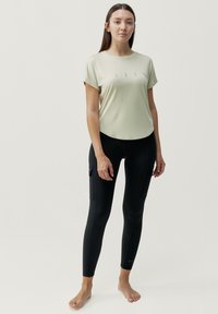 Lichtgroene sporttop met korte mouwen en een ronde halslijn, versierd met een klein bedrukt design. Deze is gecombineerd met nauwsluitende zwarte leggings met cargozakken.