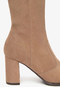Bruine nubuck enkellaars met een stevige hak, gladde textuur, gebogen silhouet en subtiele stiksels aan de zijkant.