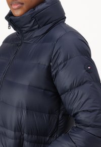 Námornická péřová bunda s vysokým límcem, zipem a prošívanou texturou. Obsahuje část s kulatou nášivkou na rukávu.