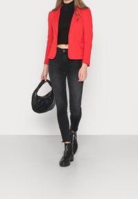 Czerwony blezer, czarny prążkowany crop top, czarne wąskie jeansy, czarne botki za kostkę z zamkiem błyskawicznym oraz czarna pikowana torebka.
