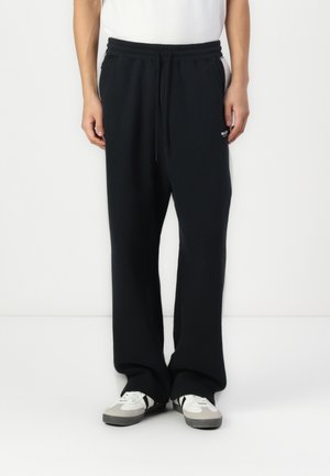 Pantalons de survêtement noirs avec une coupe décontractée, taille à cordon, poches latérales et détails de logo brodé. Associés à des baskets blanches et grises.
