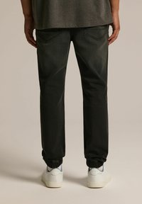 Czarne dresowe spodnie z elastycznym paskiem w talii i mankietami, o gładkiej fakturze i delikatnym wyblaknięciu. Noszone z białymi trampkami.