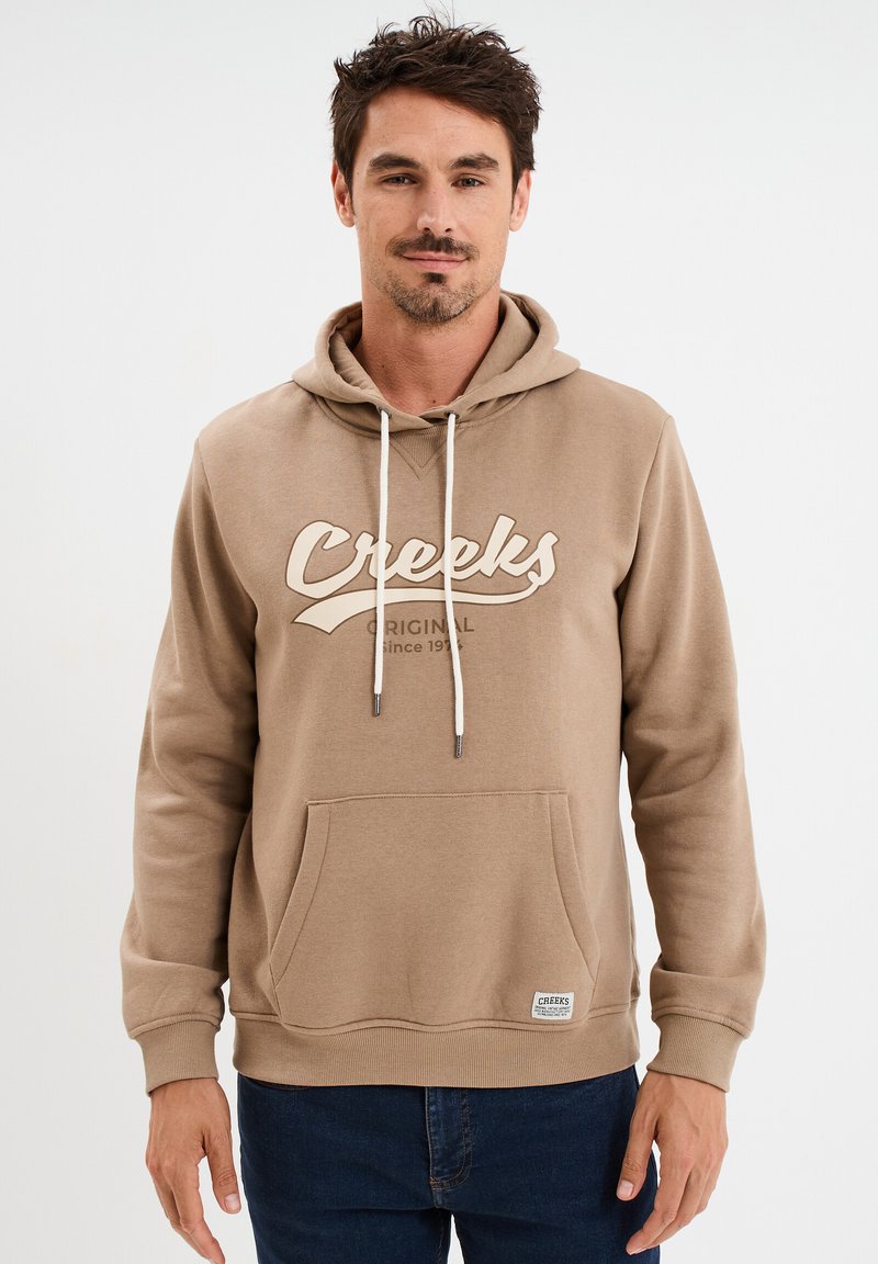 Beige Kapuzenpullover mit Fronttasche, Schnürzug und "Creeks"-Logo in Beige. Verfügt über gerippte Bündchen und Saum, aus weichem Material gefertigt.