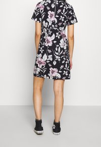 Květinové šaty s černým pozadím, krátké rukávy, po kolena, zdobené růžovými a bílými květinami. Vybaveno černými vysokými teniskami.