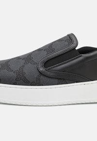 Chaussure noire à enfiler avec une tige texturée présentant un motif subtil, des panneaux latéraux élastiques et une semelle en caoutchouc blanche.