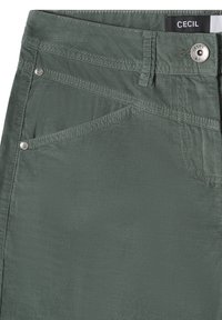 Gros plan sur un pantalon en velours côtelé vert avec poche avant, passants de ceinture, rivets argentés et fermeture par bouton métallique avec étiquette de marque "CECIL" à l'intérieur de la ceinture.