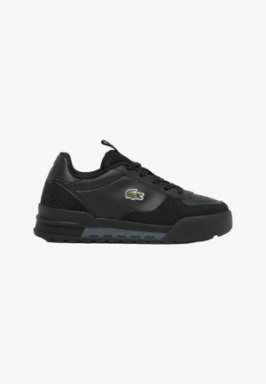 Basket noire à lacets avec semelle texturée, languette en mesh et logo crocodile vert sur le côté.