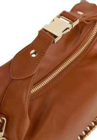 Torba iz usnjene barve tan z zlatimi dodatki, ki ima zadrgo in verižni okras. Gladka tekstura s šivanimi detajli.