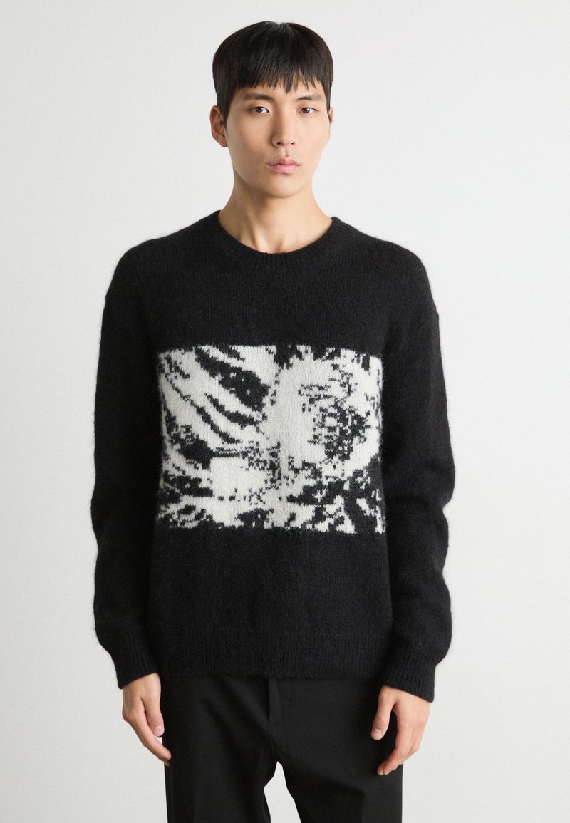 Black knitted sweater with a fuzzy texture, featuring a white and black graphic design at the center and ribbed cuffs and hem.