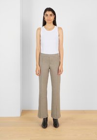 Witte geribbelde tanktop, bruine geruite hoge taille flared broek, enkel-lang, gecombineerd met zwarte puntige enkellaarzen. Minimalistische achtergrond.