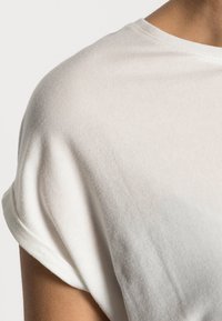 White cotton T-shirt with rolled sleeves, showing a smooth texture and slight draping. The fabric appears lightweight and breathable.