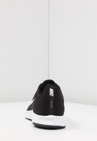 Chaussure de sport noire avec une tige en tissu en maille, semelle intermédiaire blanche et semelle extérieure noire. Présente un logo Nike blanc bien en vue et le texte "JUST DO IT".
