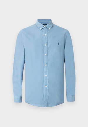 Camisa azul-claro com botões na frente, mangas compridas, colarinho pontudo e um pequeno logótipo azul-marinho no peito. Tecido em mistura de algodão com textura suave.