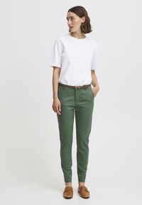 T-shirt en coton blanc associé à un pantalon vert slim, avec une ceinture marron et des mocassins marron avec une touche d'or.