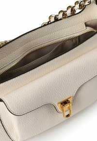 Gestructureerde crèmekleurige leren handtas met gouden hardware, kettingbandje en ritsvakken. Voorzien van een kenmerkende klepsluiting.