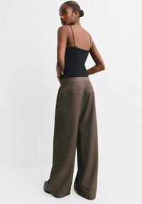 Schwarzes Tanktop mit dünnen Trägern, kombiniert mit hochtaillierten, weit geschnittenen braunen Hosen, die ein dezentes Nadelstreifenmuster und Gesäßtaschen aufweisen.