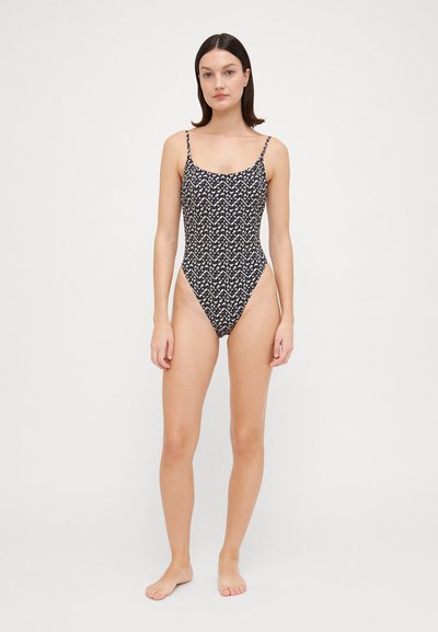 Bañador de una sola pieza negro con un patrón geométrico crema, tirantes ajustables y un diseño de pierna alta para una silueta elegante.