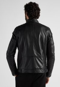 Zwarte leren jas met een gestructureerd ontwerp, geribbelde accenten op de schouders en ritsmanchetten. Soepele textuur met zichtbare stikdetails.