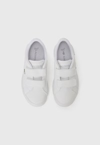 Baskets blanches avec deux bandes Velcro, en matériau synthétique lisse, forme de bout rond et semelle texturée. Logo Lacoste sur la languette.