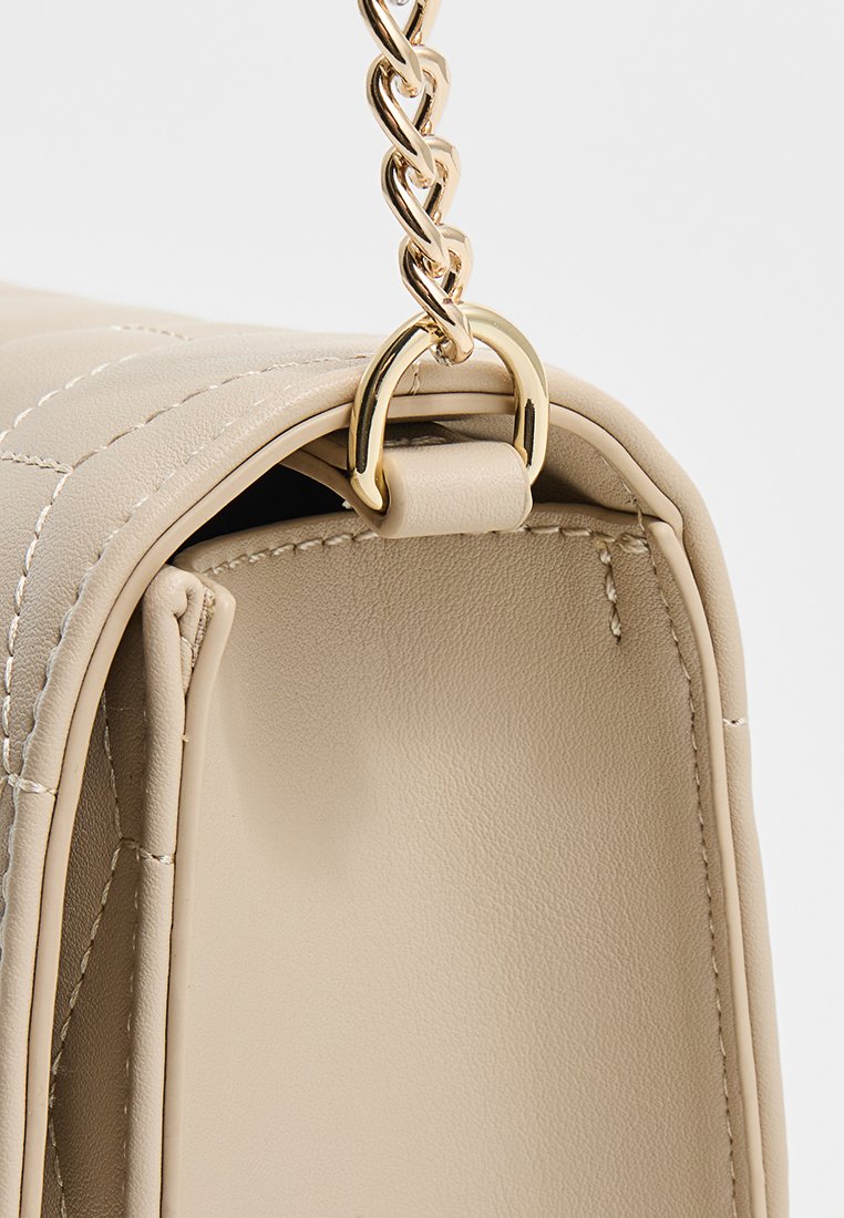 Bolso de mano de cuero acolchado beige con cadena de tono dorado y herrajes en forma de anillo, que muestra una textura suave y líneas limpias.