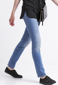 Ljust blå denimjeans med smal passform, lätt slitage vid knäet, matchade med svarta sneakers och en svart väska.