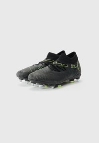 Ghete de fotbal negre cu accente verzi, partea superioară texturată și guler de tip șosetă. Dispune de ținte conice pe o talpă flexibilă pentru aderență.