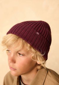 Burgundy ribbed beanie hat made of soft knit material, featuring a small logo tag and a close-fitting design.