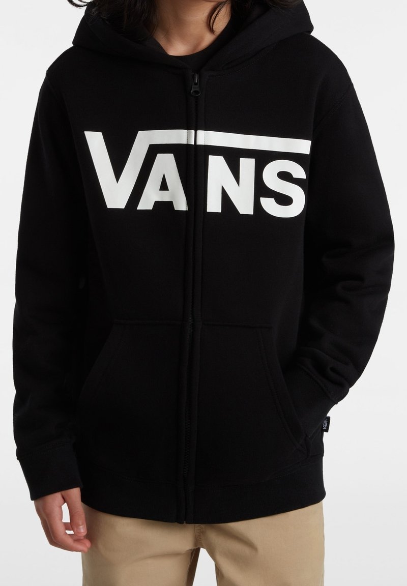 Hoodie noir Vans avec un logo blanc sur la poitrine, fermeture éclair sur le devant, deux poches et une capuche avec cordon de serrage. Texture de tissu douce.