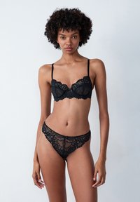 Set di reggiseno e perizoma in pizzo nero con motivi floreali, bordi scallop e spalline regolabili. Design trasparente e dettagliato.