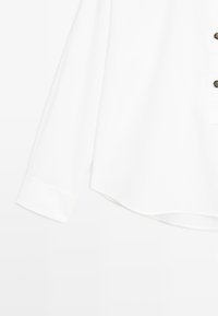 Chemise blanche à manches longues avec poignets boutonnés, patte de boutonnage partielle avec boutons décoratifs et ourlet incurvé.