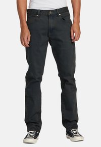 Vaqueros de mezclilla negra con diseño de pierna recta, con cremallera y cierre de botón, cinco bolsillos y un leve desgastado. Combinados con zapatillas negras.