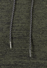 Gebreide hoodie in donkergroen met een gestructureerd patroon; voorzien van een zwarte trekkoord met witte stippen en metalen aglets.
