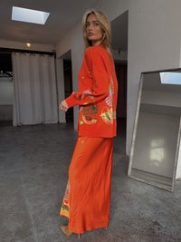Sweater laranja em malha com padrões florais, combinado com uma saia maxi laranja a condizer. Textura suave e design longo e fluido.